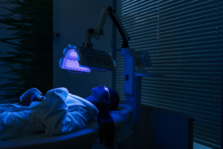Remote view of female patient undergoes blue LED light therapy for skin rejuvenation at mo