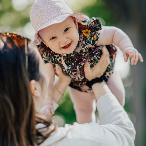 Børnefotografering i Jylland – Mor løfter sin baby op i luften og smiler.