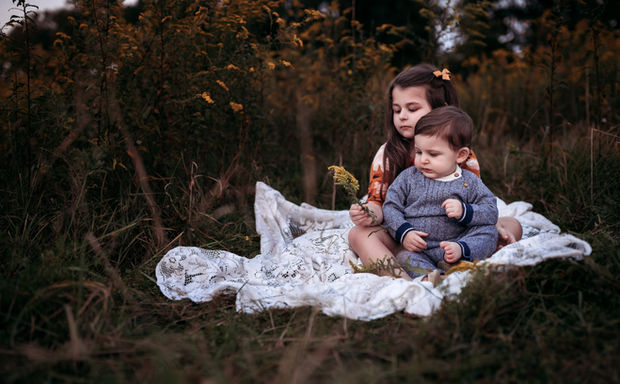 sister and baby cuddled together in a lifestyle family photo on a white lace blanket in a tall field