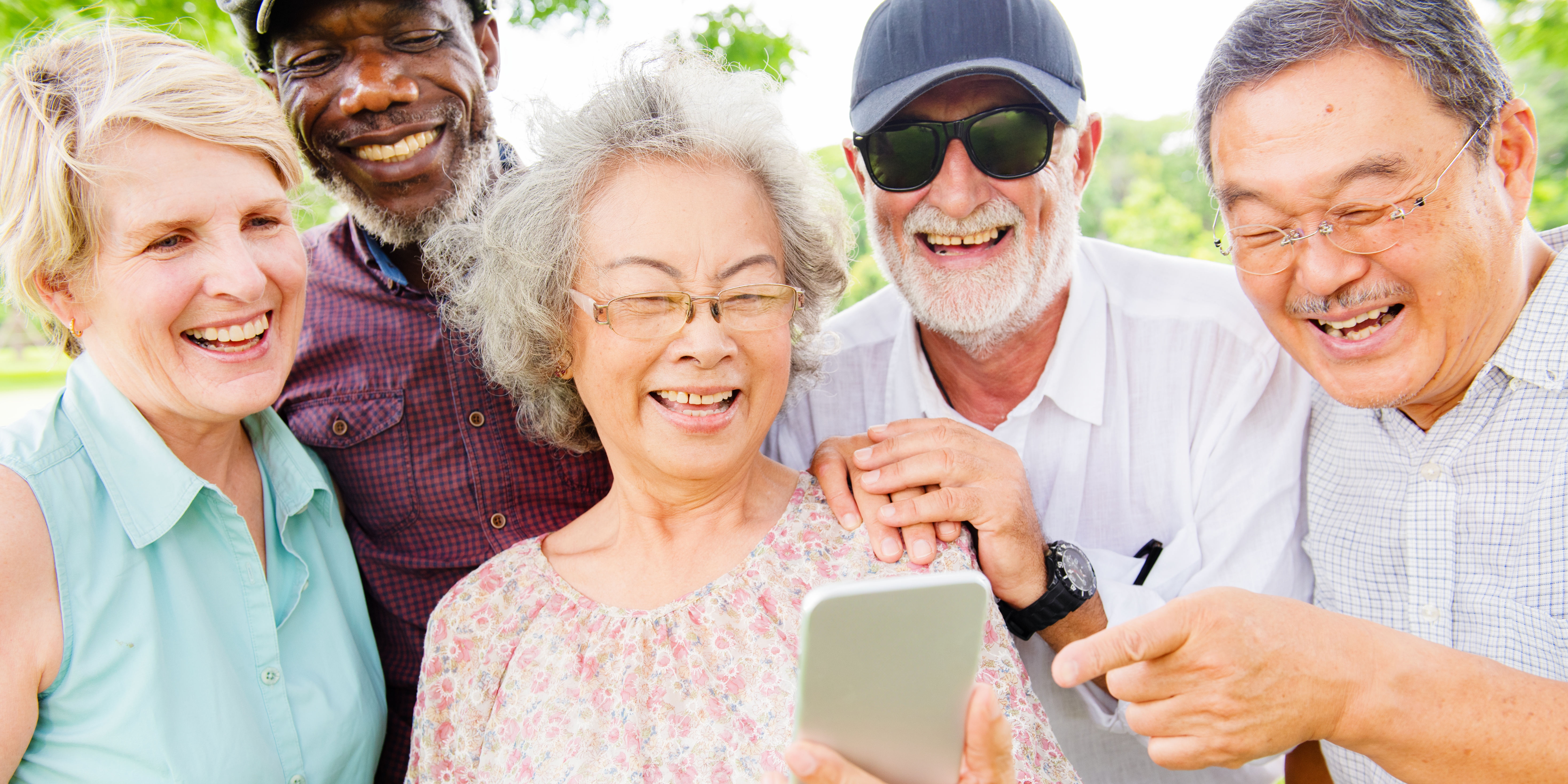 Five smiling older friends gathered outdoors around a phone
