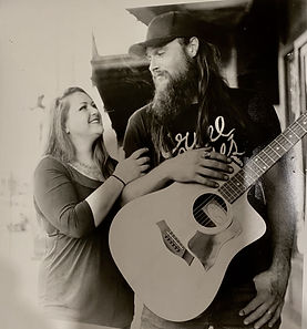 A film, black and white photo of Amberle and Tony. Tony has his guitar hanging on his chest and Amberle is holding onto Tone's arm and staring into his face with a smile.