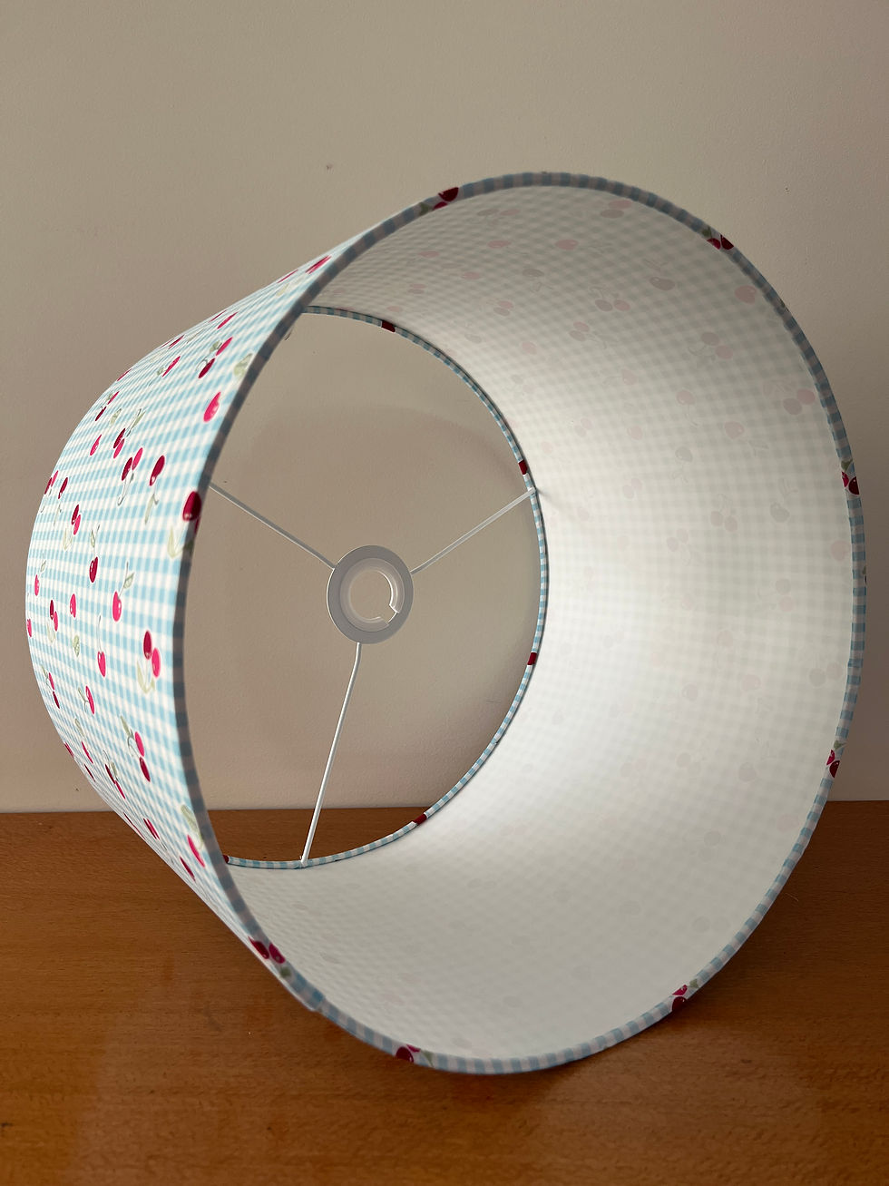 Interior of blue gingham lampshade with scattered cherry motifs showing white PVC lining.
