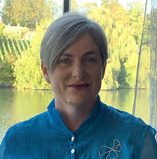 A photo of Catherine Abraham. She has short grey hair and is wearing a teal blue collared shirt.