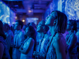 Event Attendees in a dimly lit, blue-toned, intently immersive experience. Attendees wear lanyards, creating a focused, engaged atmosphere.