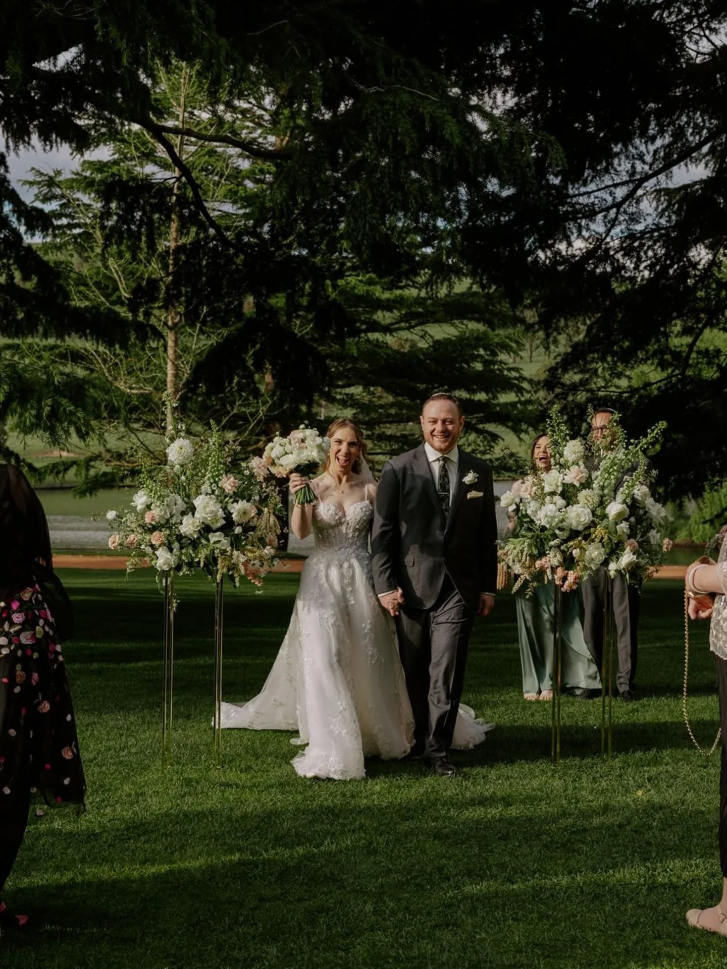 bride and groom making there ceremony exit with big flower arrangements behind them, white and green flowers