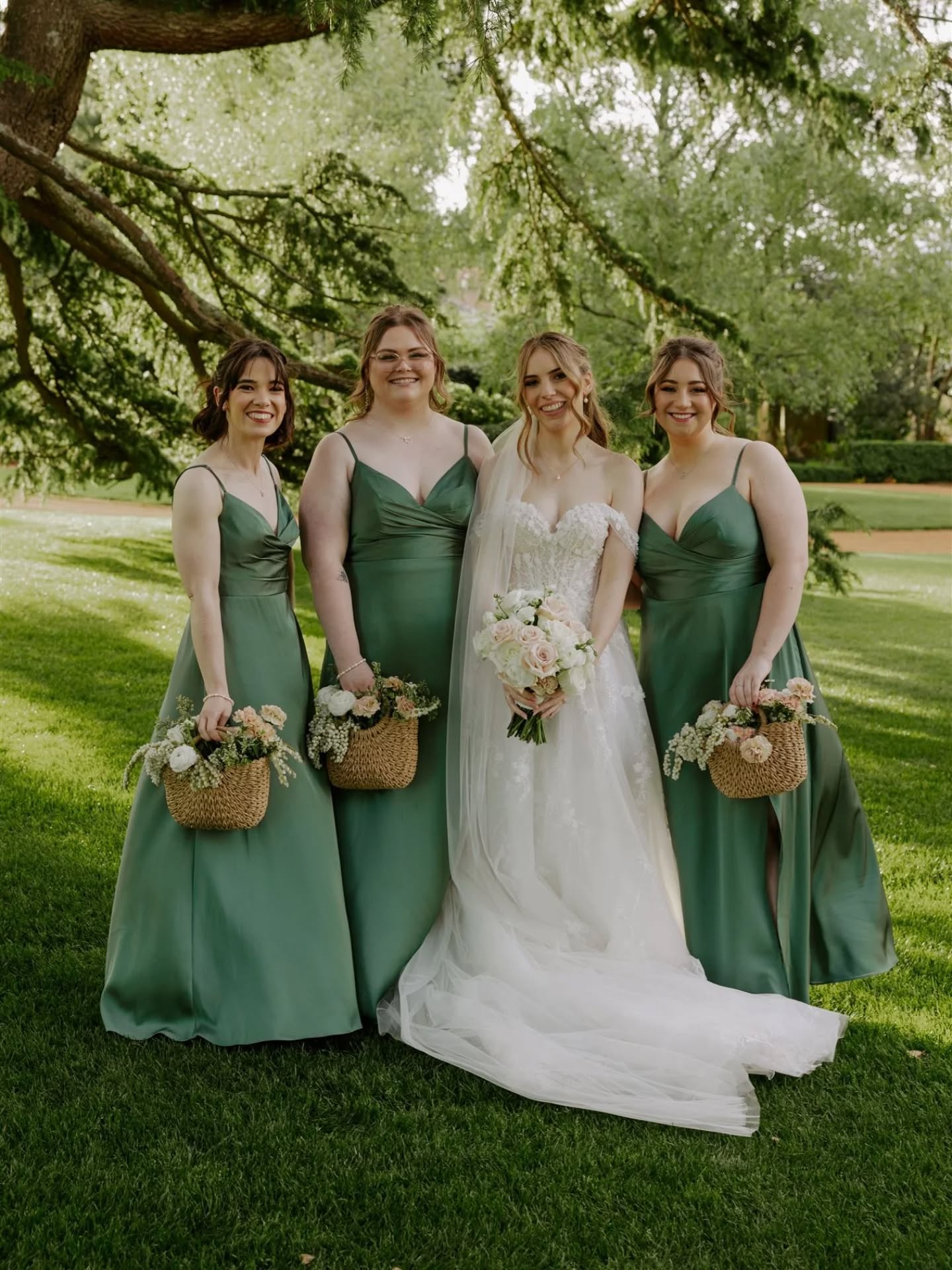 Bride standing with her bridesmaids, bridesmaids holding basket bouquets and wearing green dresses