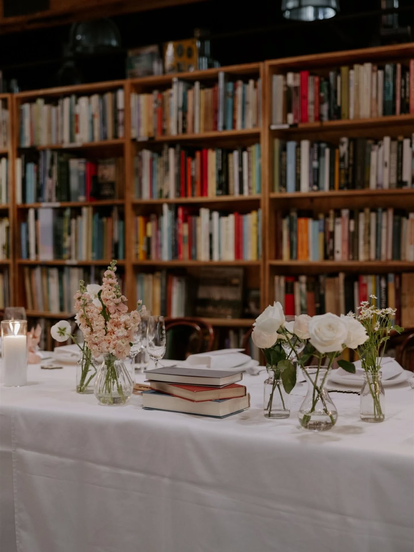 bridal table with bookshelf behind, on table books scattered with bud vases of flowers