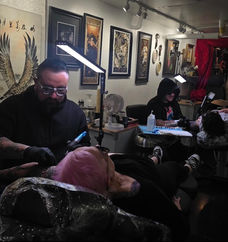 Tattoo artists tattooing clients in a studio with artwork on the walls.