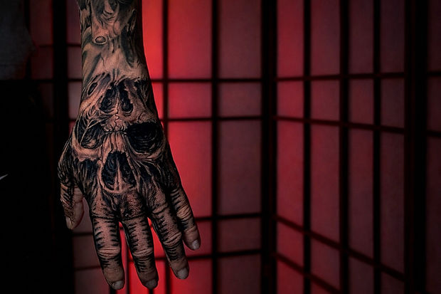 Hand with detailed skull BLACK AND GREY TATTOOS; red background grid frame.
