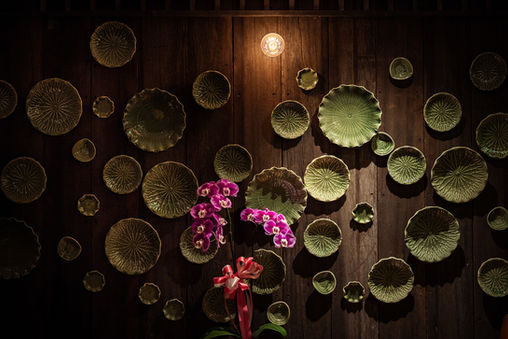 Wall installation of green ceramic plates with a pink orchid arrangement beneath warm spotlighting in a Sukhumvit soju bar interior.