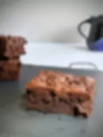 A close-up image of a thick brownie with a stack of brownies in the background.
