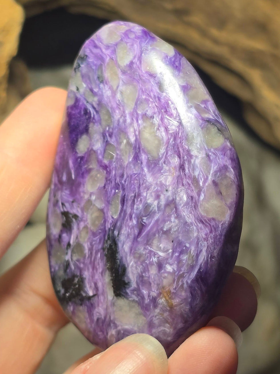 Thumbnail: polished charoite pebble hand held side view