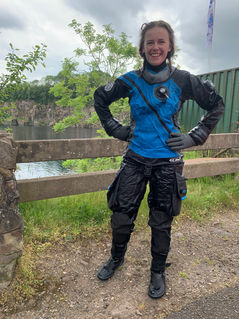 Wearing a blue, black and grey drysuit to keep me dry when diving, and smiling at the camera