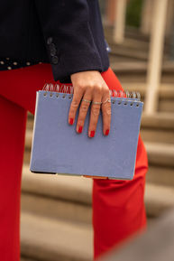 Rachel walking up some steps with a close up of her holding a 'Project Book' with red nails and rings.