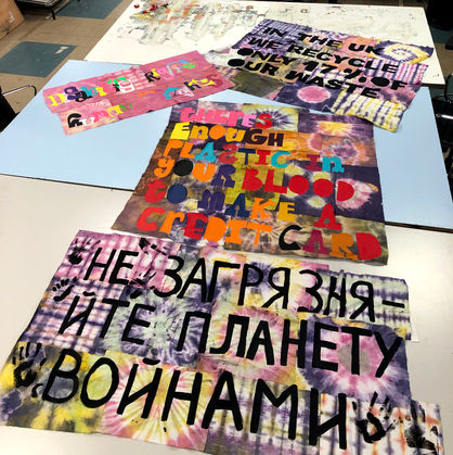 4 protest banners lie on a large table. They are socially and environmentally engaged with slogans saying "Disability rights are human rights" "In the UK we recycle only 17% of our waste" "There's enough plastic in your blood to make a credit card" and the last one is written in Ukranian and says "Stop polluting our world with wars". The banners are colourful having been dyed with a variety of plants and the type has been made from multicoloured heatpress vinyl.