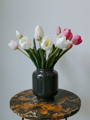 Vaas grijs met een bundeltje lichtroze Tulpen, een bundeltje donkerroze Tulpen en een bundeltje witte Tulpen.