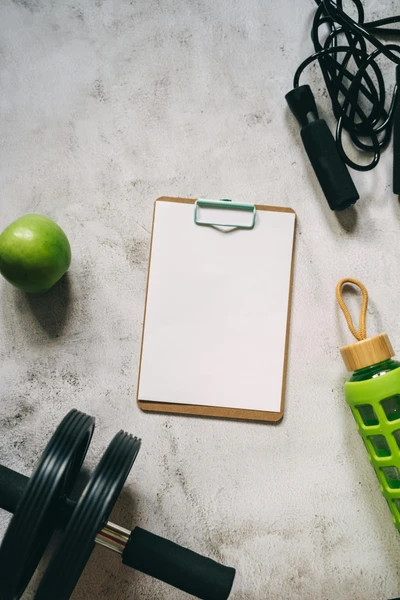 Overhead view of a clipboard with paper on the floor, surrounded by a apple, a water tumbler, an