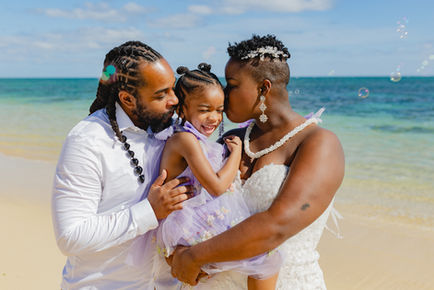 Parents and daughter sharing a joyful hug during a vow renewal on the beach in Oahu