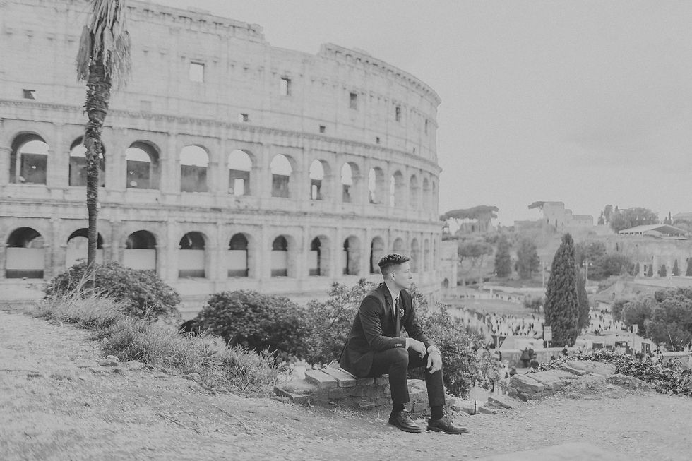 Black-and-white groom portrait seated near the Colosseum in Rome.