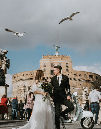 Bride and groom in editorial wedding portraits on Ponte Sant’Angelo with Castel Sant’Angelo in the background, Rome.