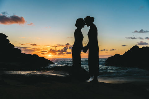 Silhouette of two brides sharing a honi (traditional Hawaiian nose-to-nose greeting) at sunrise on the lava rocks of Eternity Beach, Oahu during their wedding session. 