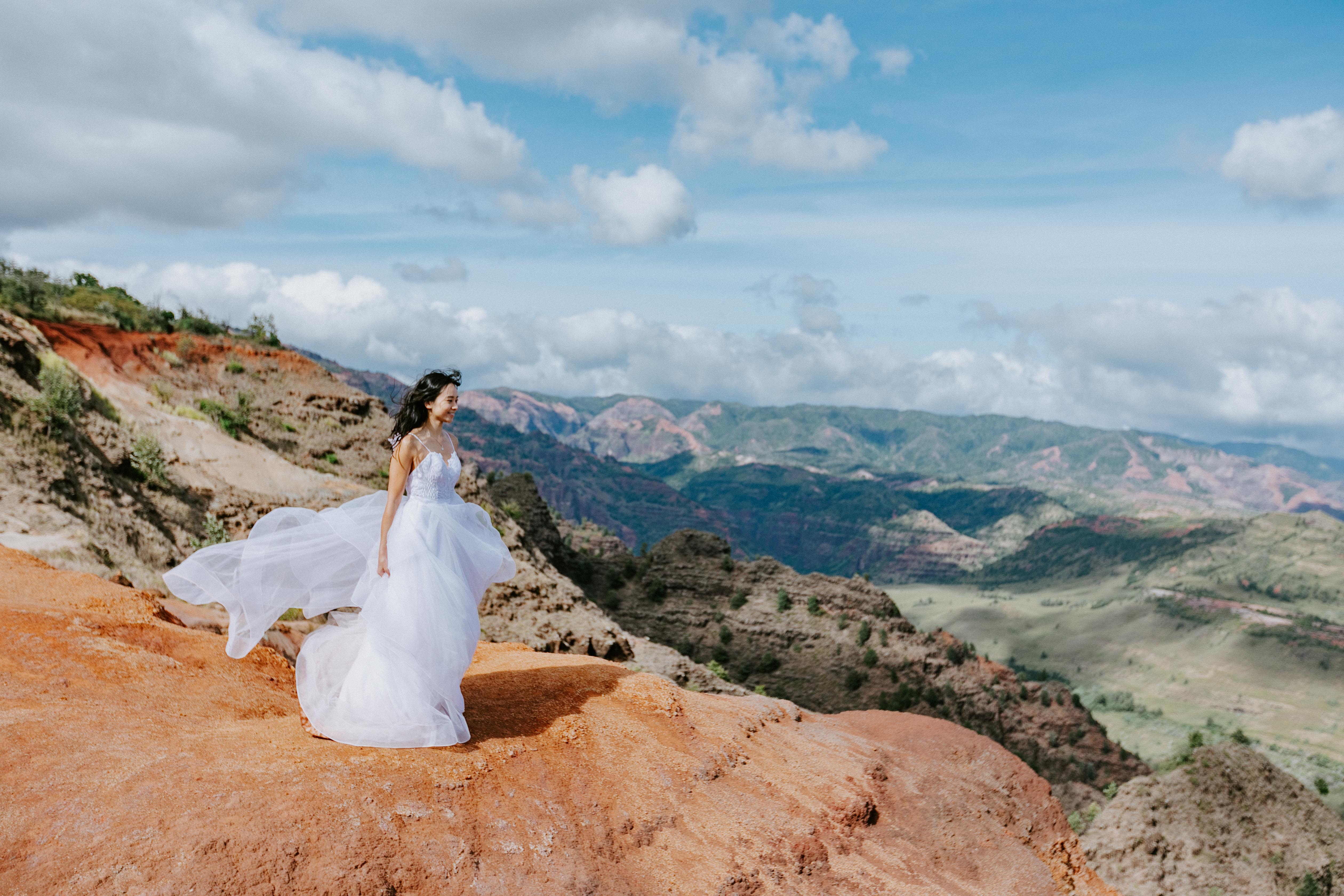 An adventurous bride stands on the edge of Waimea Canyon in Kauai during her adventure wedding sessi