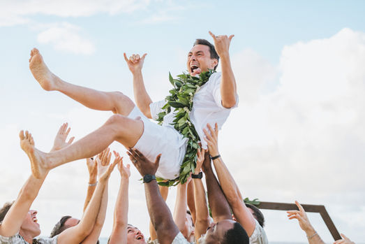 A groom gets tossed into the air while throwing shakas on his wedding day.