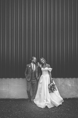 Jordan and Alexa posing in wedding attire against a textured wall