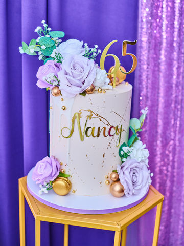 Custom purple and gold 65th birthday cake with floral décor on a gold stand, styled for an event in Long Island or NYC