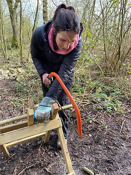 a picture of a forest school practitioner cutting wood with a bow saw