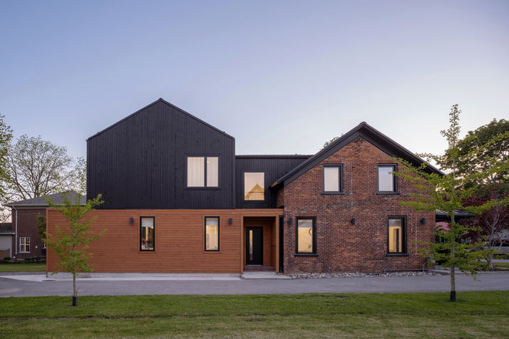 modern addition to heritage brick house with black roof and wood siding