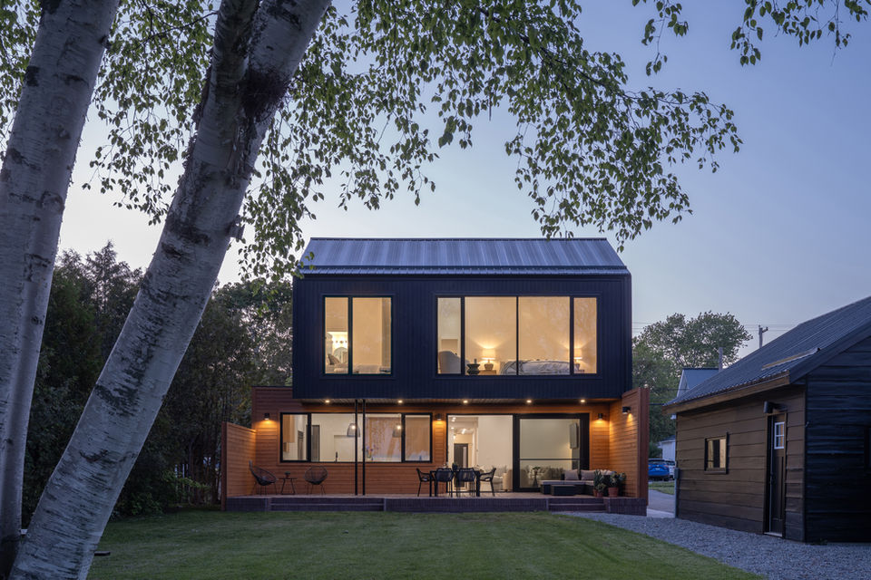 black siding modern house with cantilevered second floor at night with big windows