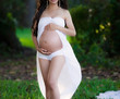 A lady who is standing outside holding her stomach to highlight she is pregnant