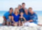 Multi-generation family seated together on white sand with the ocean behind them at Fort Lauderdale Beach, FL.