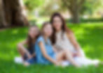 Woman seated on green grass with two girls during a relaxed family portrait in Weston, FL.