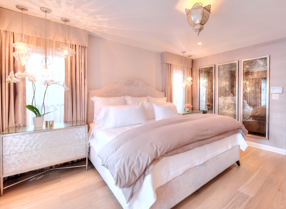 The luxurious Los Angeles  Primary Bedroom in a hotel style is a mushroom pink color, the walls, drapery and suede upholstered headboard all the same hue of color. Three antique mercury wall mirrors subtly reflect the courtyard into the moroccan styled bedroom