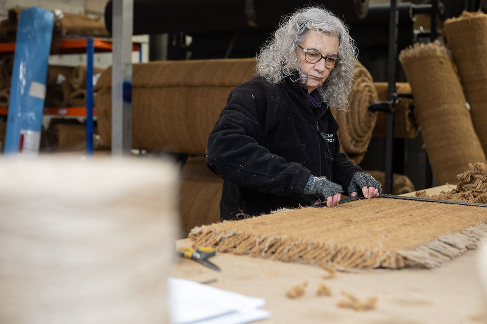 Woman cuts door mat in a workshop, surrounded by rolled mats and tools