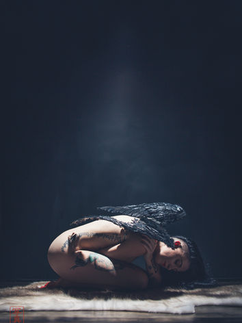 Minimalist cinematic portrait of a person curled on the floor in a dark room with a beam of cool light above.