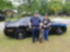 a trained dog with two security officers, in front of their vehicle.