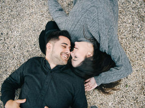 A man and a woman laying on the ground playfully touching their nose together.