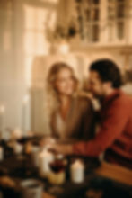 A couple shares a happy moment at a candlelit dinner table with wine. Warm, cozy setting with soft lighting and a background with plants.