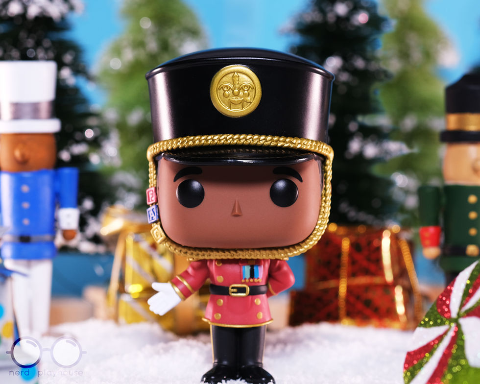Creative toy photography of Funko POP FAO Schwarz Toy Soldier standing on snow in front of trees, presents and wooden nutcracker figures.