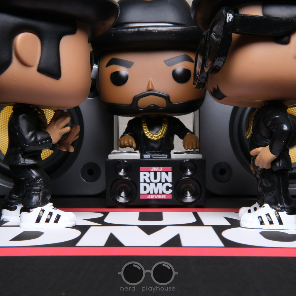 Creative toy photography of Funko POP Run-DMC in front of a pair of large desk speakers.