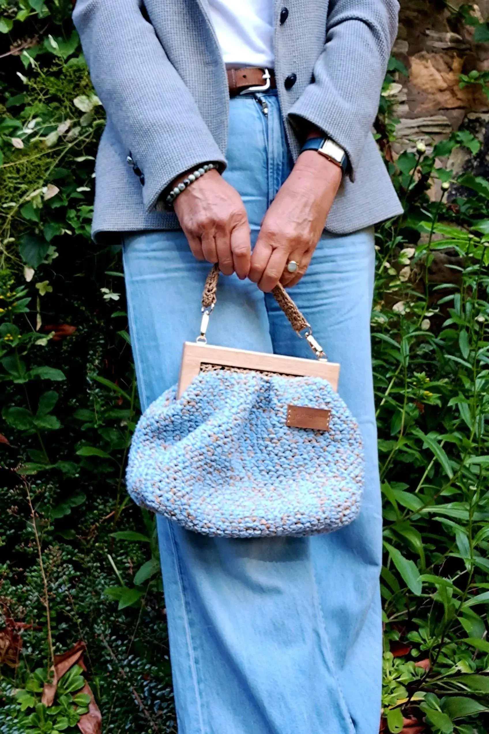 Pale blue cotton & raffia purse bag with wooden handles & raffia straps shown held by model. Structured lined purse bag