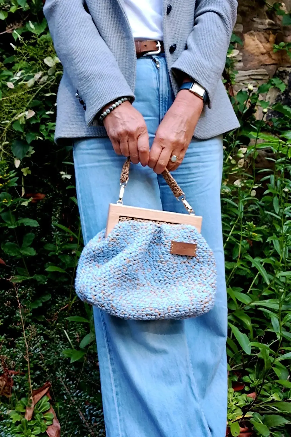 Pale blue cotton & raffia purse bag with wooden handles & raffia straps shown held by model. Structured lined purse bag