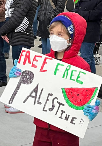 A child wearing face mask holding a sign that reads" Free free Palestine" and a drawing of a watermelon