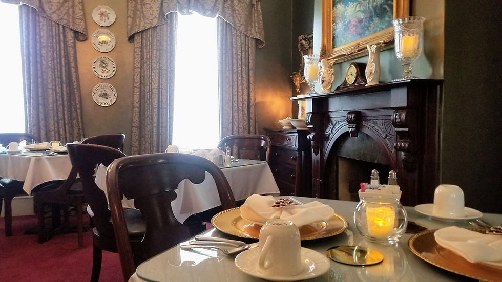 Elegant dining room with a cozy, vintage feel. White tablecloths, gold plates, and candlelit tables. Ornate fireplace and floral curtains. Warm ambiance.