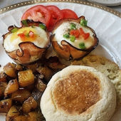 Sliced fresh tomatoes, seasoned rosemary potatoes, a toasted English muffin, and savory baked ham and egg crisps served fresh at an outstanding historic bed and breakfast.