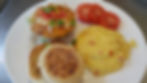 Plate with a Southwestern Eggs, tomato slices, cheesy grits, and an English muffin. Bright colors on a white plate.