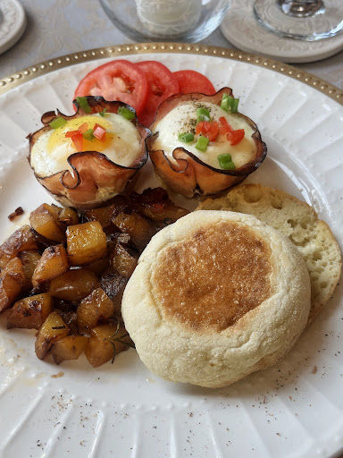 Sliced fresh tomatoes, seasoned rosemary potatoes, a toasted English muffin, and savory baked ham and egg crisps served fresh at an outstanding historic bed and breakfast.